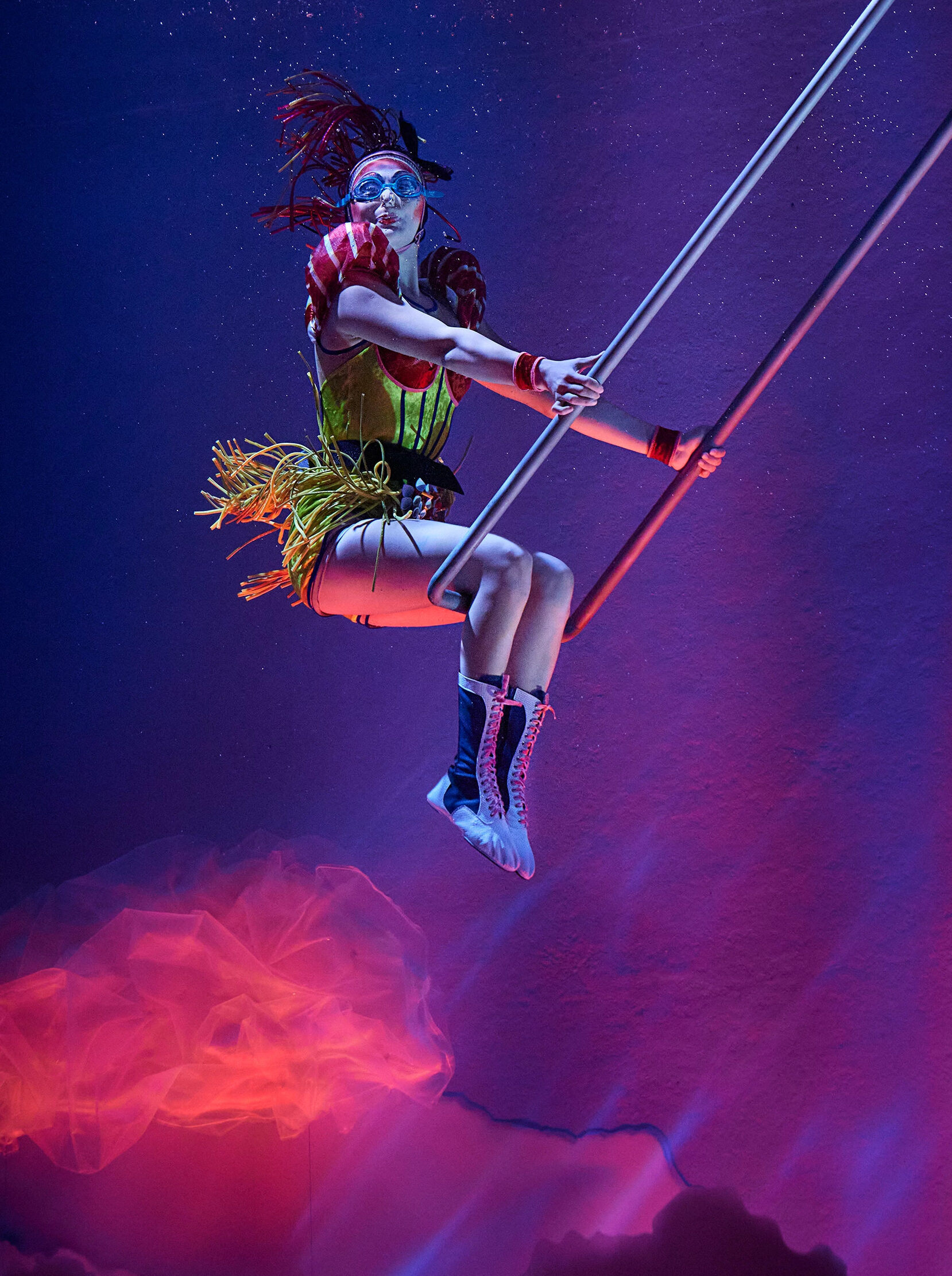 Acrobat underwater trapeze act performed in audience surrounding performer aquariums.